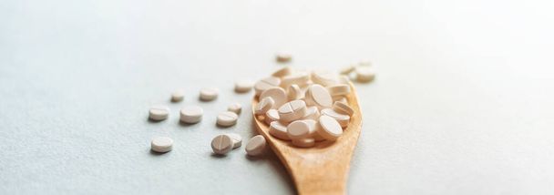 Close-up white pills, tablets in wooden spoon on blue table. Medicine and health concept. pharmaceutics. Top view. Pills and vitamins - 写真・画像