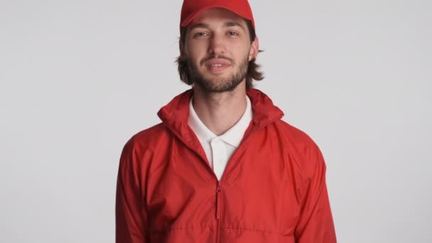 Retrato de cara de entrega sorridente em boné vermelho e casaco olhando alegremente na câmera sobre fundo branco. Conceito de serviço - Filmagem, Vídeo