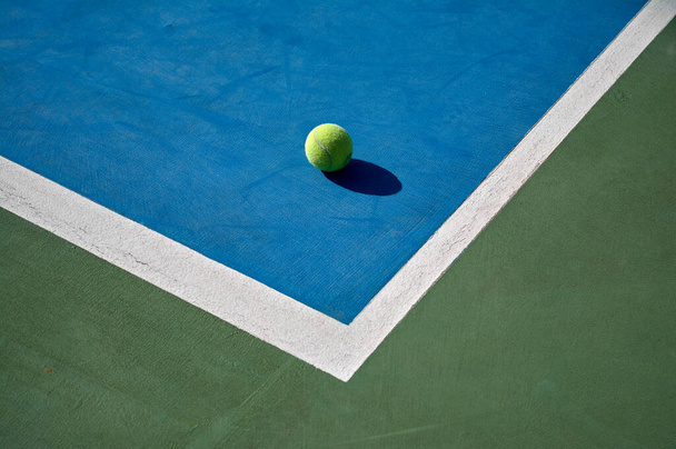 detail van een gele tennisbal op de hoek van een blauwe baan met witte lijnen en groene buitenkant - Foto, afbeelding