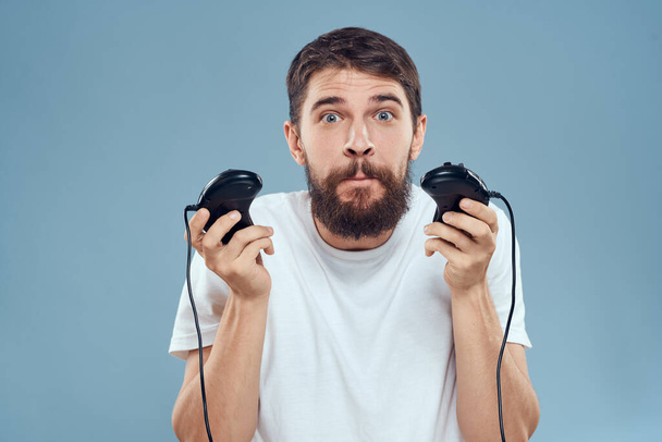man holding gamepads games lifestyle technology console emotions white t-shirt blue background - Zdjęcie, obraz