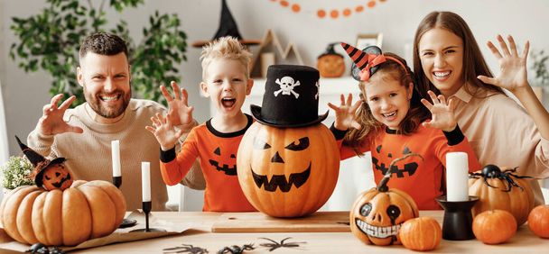 幸せな両親とカボチャのジャックOランタンジェスチャーと子供たちは、自宅でキッチンでハロウィーンのお祝い中にカメラのための恐ろしい顔を作ります - 写真・画像