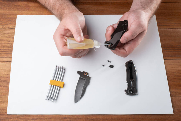Man lubricating the compounds of a pocket knife with household oil - Foto, afbeelding
