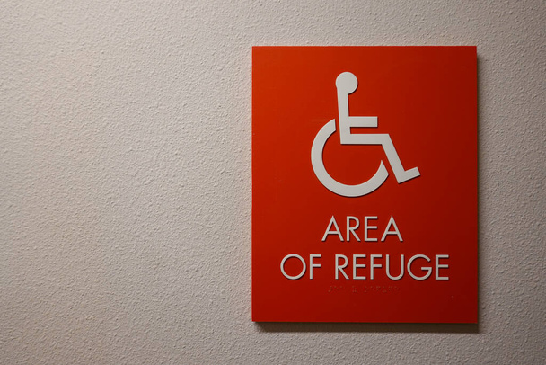 Une pancarte dans un couloir d'un complexe d'appartements qui dit Zone de refuge avec un symbole de fauteuil roulant sur elle qui est une zone de rassemblement d'urgence pour les personnes handicapées. - Photo, image