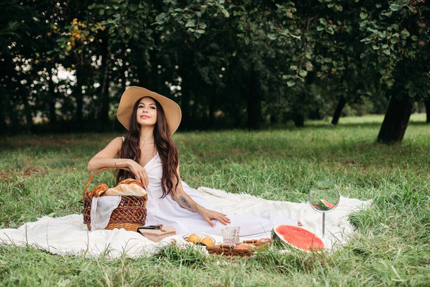 Portret młodej pięknej dziewczyny z białymi zębami, piękny uśmiech w słomkowym kapeluszu i długa biała sukienka mają piknik w ogrodzie - Zdjęcie, obraz
