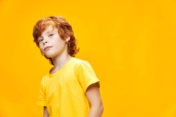 Neşeli kızıl saçlı çocuk, elleri tişörtlü, yüzle ilgili bir yüz ifadesiyle el kol hareketi yapıyor. - Fotoğraf, Görsel