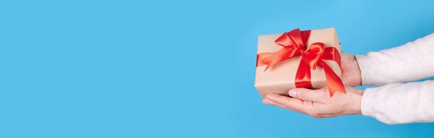 Present box with red ribbon in hands on blue background. - Photo, Image
