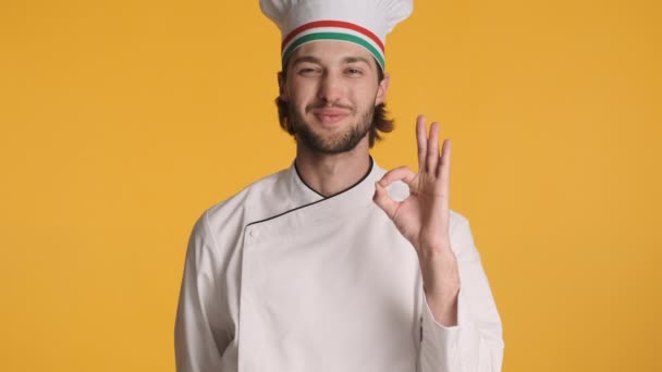 Houkutteleva ammatillinen italialainen kokki yhtenäinen iloisesti osoittaa ok ja bellissimo ele yli värikäs tausta. Hyvin tehty. - Materiaali, video
