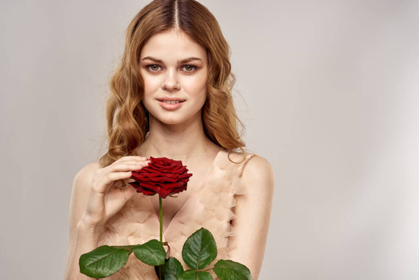 Portrait of a beautiful woman with a red rose on a beige background cropped view of an evening dress - Photo, Image