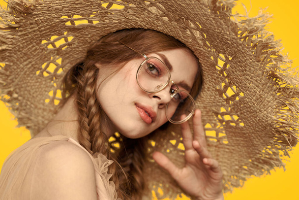 Saçları örgülü ve sarı arka planda şapkası olan güzel bir kadının portresi. - Fotoğraf, Görsel