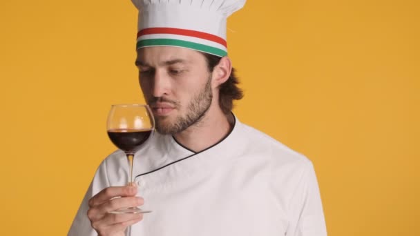 Professionele Italiaanse chef-kok in uniform vol vertrouwen ruiken wijn tonen bellissimo gebaar op camera over kleurrijke achtergrond. Sommelier-concept - Video