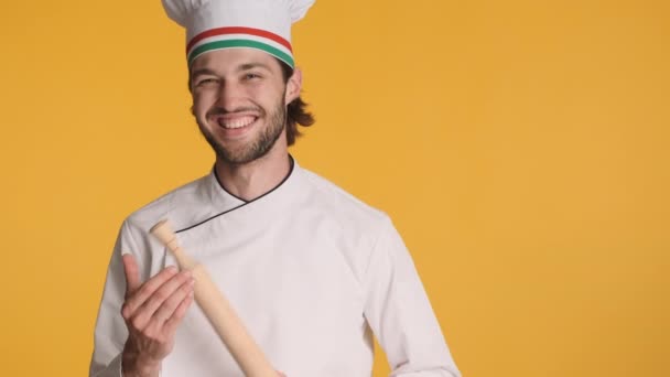 Profesional chef italiano alegre en uniforme con rodillo alegremente mostrando el gesto de pulgar hacia arriba en la cámara sobre el fondo colorido - Metraje, vídeo