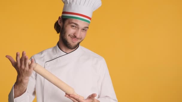 Profesionální pohledný italský kuchař v uniformě s válcování pin šťastně ukazuje Bellissimo gesto na fotoaparátu přes barevné pozadí - Záběry, video