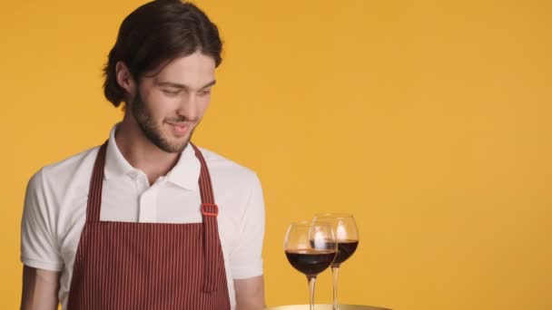 Joven camarero excitado atractivo sosteniendo bandeja con vino tinto sorprendentemente mirando en la cámara sobre fondo colorido - Metraje, vídeo