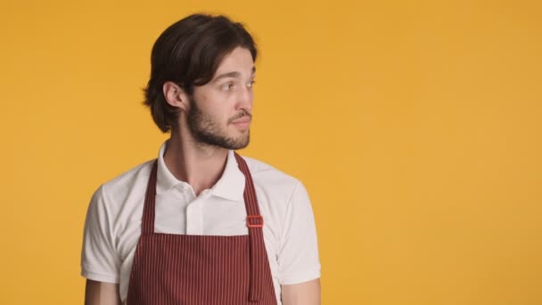 Young attractive surprised waiter looking aside on copy space and pointing fingers over colorful background. Copy space - Footage, Video