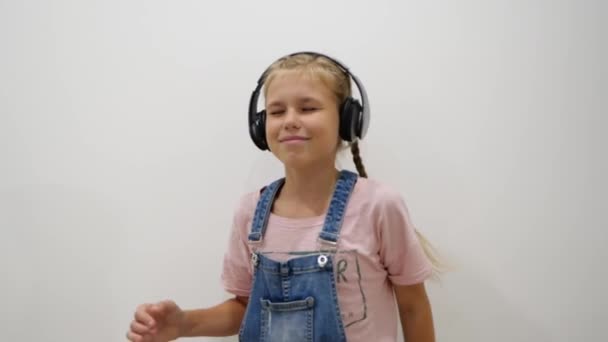 Jolie jeune fille qui s'amuse, sourit, danse avec des écouteurs sur fond blanc. Musique, danse, concept radio, ralenti - Séquence, vidéo