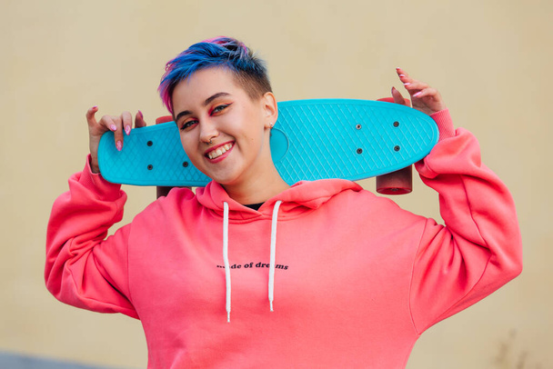 Stylish young woman holding skateboard on her shoulders. Youth concept. - Foto, afbeelding