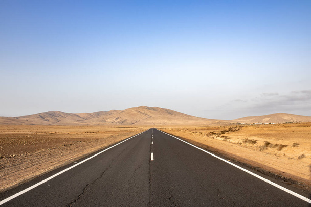 deserted road with mountains in the background in arid landscape on Fuerteventura canary islands - 写真・画像