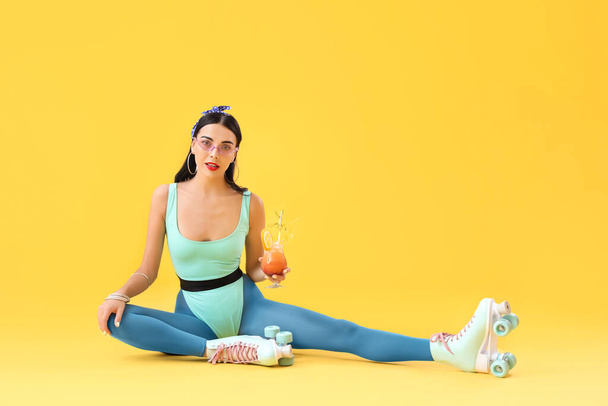 Beautiful young woman on roller skates and with cocktail against color background - Foto, imagen