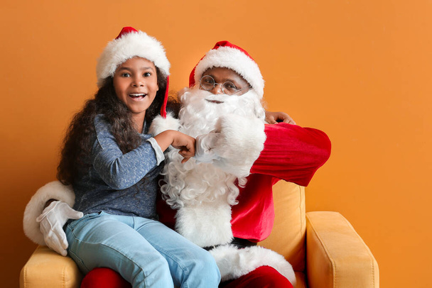 Afro-amerikanische Weihnachtsmann mit niedlichen kleinen Mädchen schlägt Fäuste auf farbigem Hintergrund - Foto, Bild