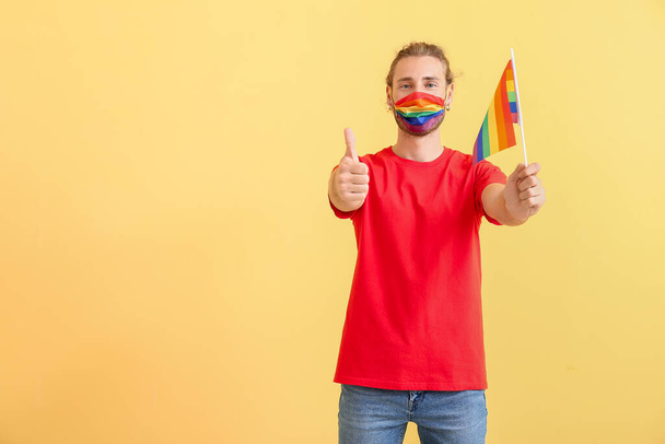 Junger Mann mit LGBT-Flagge zeigt Daumen hoch auf farbigem Hintergrund - Foto, Bild