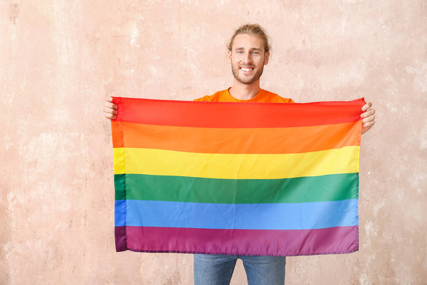 Young man with LGBT flag on color background - Photo, Image