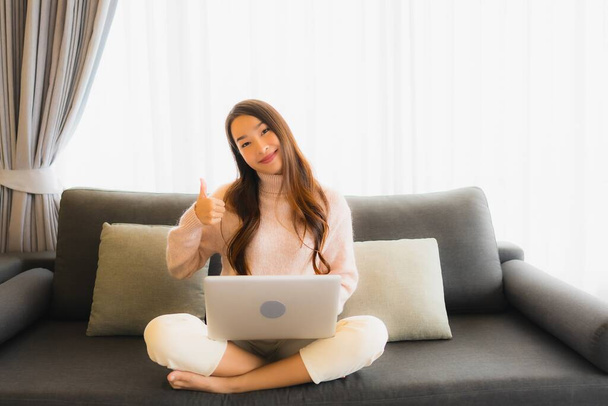 Retrato hermosa joven mujer asiática utilizando el ordenador portátil para el trabajo en el sofá en el interior de la sala de estar
 - Foto, Imagen