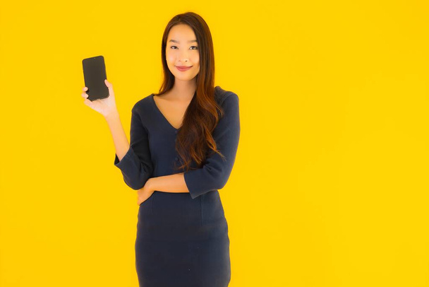 Muotokuva kaunis nuori aasialainen nainen älypuhelimella tai matkapuhelimella keltaisella eristetyllä taustalla
 - Valokuva, kuva