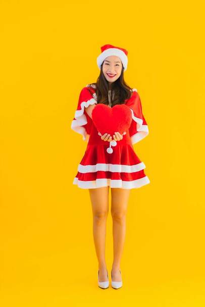 Retrato hermoso joven asiático navidad ropa y sombrero sonrisa feliz con forma de corazón en amarillo aislado fondo
 - Foto, imagen