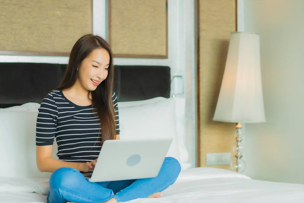 Портрет красивая молодая азиатская женщина использовать компьютер ноутбук на кровати в интерьере спальни - Фото, изображение