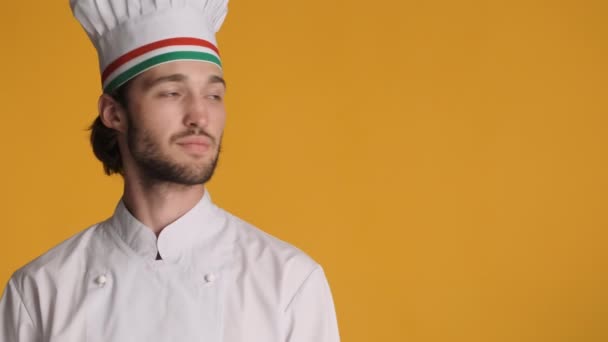 Atraktivní profesionální kuchař v uniformě úžasně při pohledu stranou na kopírovací prostor a šťastně ukazující palec nahoru přes barevné pozadí - Záběry, video