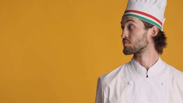 Fešák profesionální kuchař v uniformě úžasně dívá stranou na kopírovací prostor a ukazující palec nahoru gesto přes barevné pozadí - Záběry, video