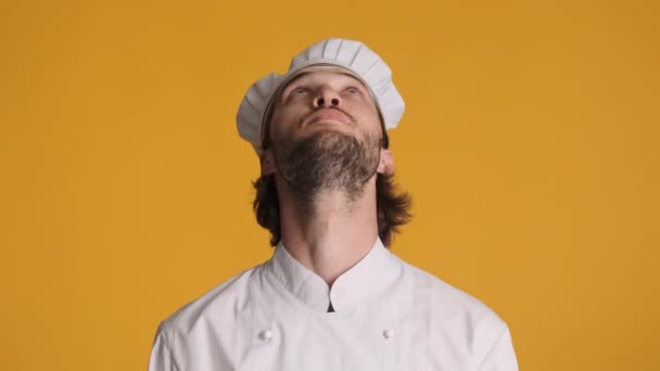 Atractivo chef profesional en uniforme asombradamente mirando en la cámara que muestra el gesto de mirar hacia arriba sobre el fondo colorido. Wow expresión - Metraje, vídeo