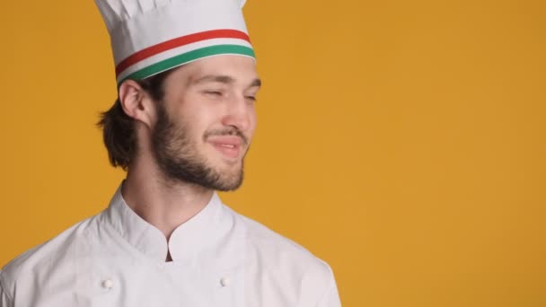 Przystojny uśmiechnięty profesjonalny kucharz w mundurze szczęśliwie patrząc na przestrzeń kopiowania na kolorowe tło. Miejsce na tekst - Materiał filmowy, wideo