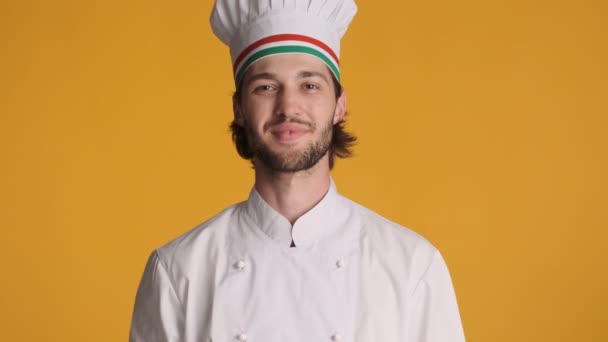 Fešák profesionální italský kuchař v uniformě drží rajčata a makaróny šťastně se usmívá na kameru přes barevné pozadí - Záběry, video