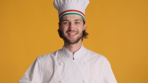 Schöner italienischer Koch in Uniform, der aufgeregt Tomaten und Makkaroni vor buntem Hintergrund in die Kamera zwinkert - Filmmaterial, Video