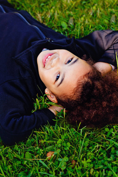 Afro-American little girl lying on green grass - 写真・画像