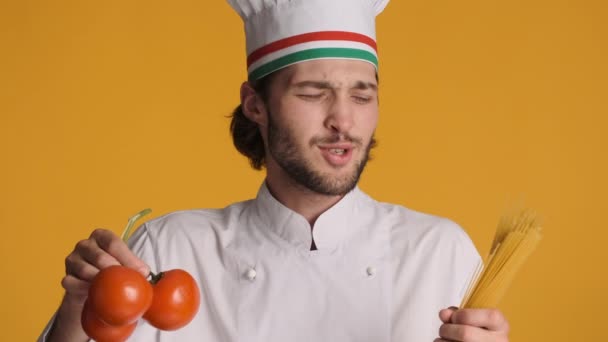 Muotokuva komea italialainen kokki yhtenäinen tilalla tuoreita tomaatteja ja makaronia iloisesti laulaa yli värikäs tausta - Materiaali, video