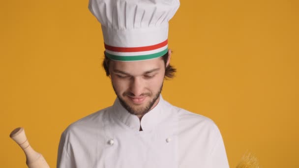 Portret van aantrekkelijke Italiaanse chef-kok in uniform met rollende pin en macaroni verbazingwekkend kijkend in camera over kleurrijke achtergrond - Video
