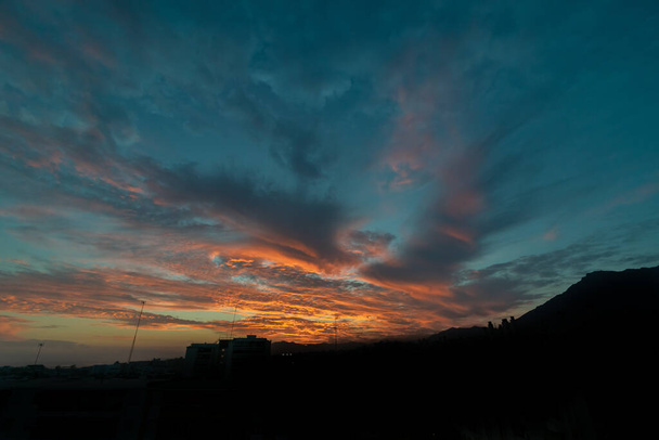 poslední sluneční paprsky vycházející zpoza horské siluety osvětlující mraky nad Marbellou - Fotografie, Obrázek