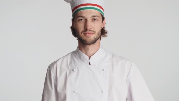 Atractivo chef italiano en uniforme mostrando felizmente tomate fresco y cuchillo en la cámara sobre fondo blanco - Imágenes, Vídeo