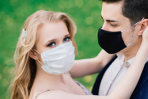 Młoda kochająca się para spacerująca w maskach medycznych w parku podczas kwarantanny w dniu ślubu. Koronawirus, choroba, ochrona, choroba. Święto Europy odwołane. - Zdjęcie, obraz