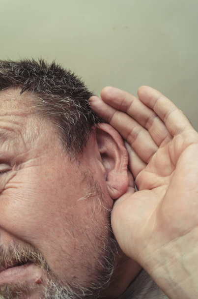 Retrato inusual de un hombre escuchando a escondidas. Un adulto con barba se puso una mano abierta en la oreja. Expresiones faciales y emociones. - Foto, imagen