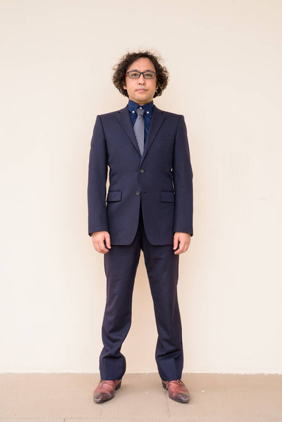 Portrait of Japanese businessman with curly hair wearing suit against concrete wall - Fotó, kép