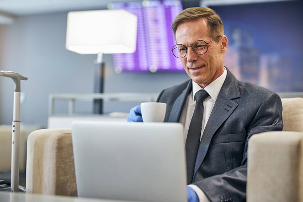 Smiling businessman relaxing with laptop in airport lounge - Foto, afbeelding