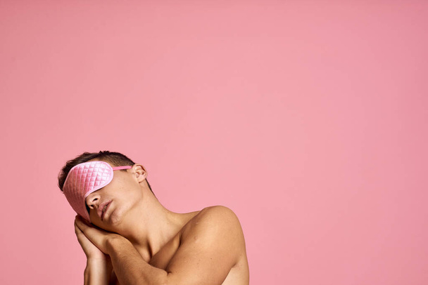 man in pink sleep mask on pink background naked shoulders morning - Foto, Imagen