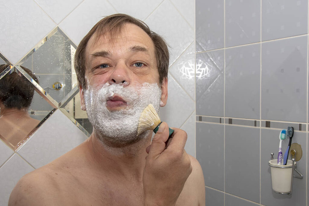 Mężczyzna rozprowadza krem do golenia na twarzy szczotką do golenia.. - Zdjęcie, obraz