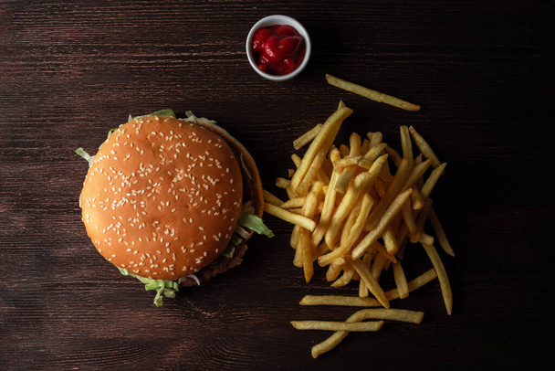close-up of a hamburger and a pile of French fries on a wooden background - Фото, изображение