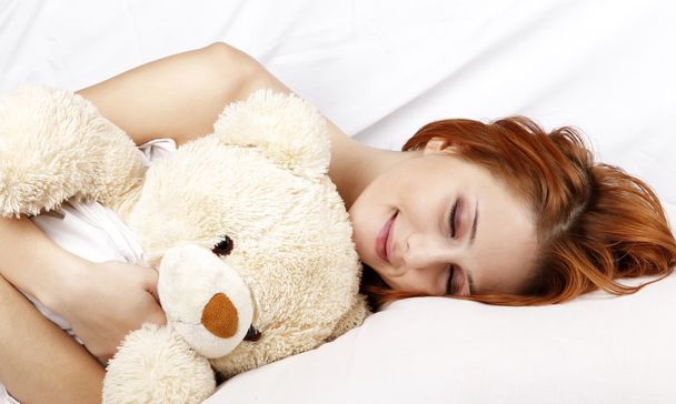 γυναίκα στο λευκό nightie ξαπλωμένη στο κρεβάτι με μαλακό παιχνίδι. - Φωτογραφία, εικόνα