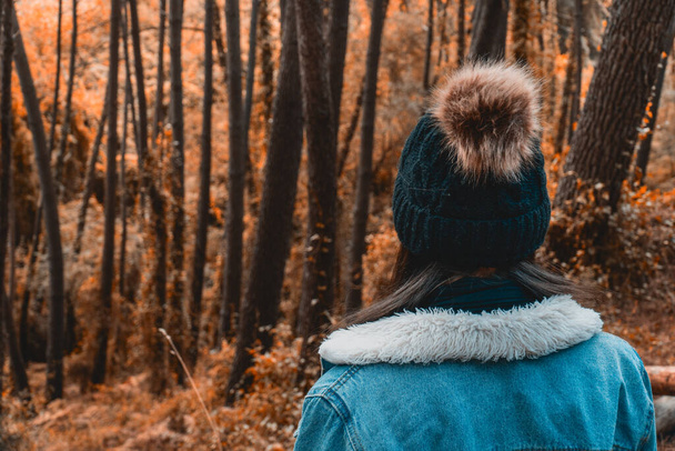 Mujer joven mirando a través de un bosque de colores de otoño con ropa de temporada - Foto, imagen