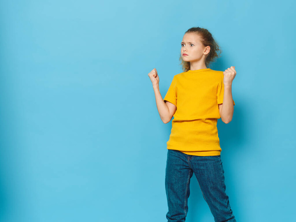Ein aufgeregtes Mädchen in gelbem T-Shirt und Jeans auf blauem Hintergrund - Foto, Bild